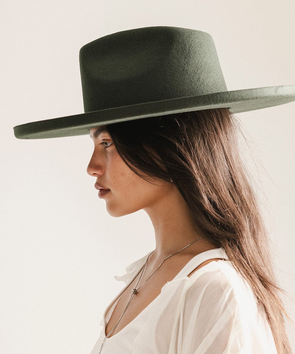 Woman wearing a dark green wide-brimmed hat against a plain background #color_dark green