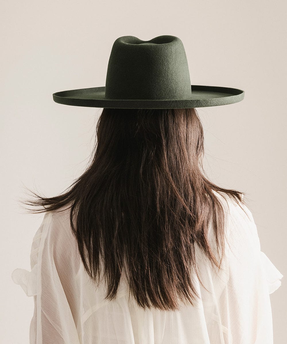 Person wearing a dark green hat with long hair and a light shirt on a neutral background #color_dark green