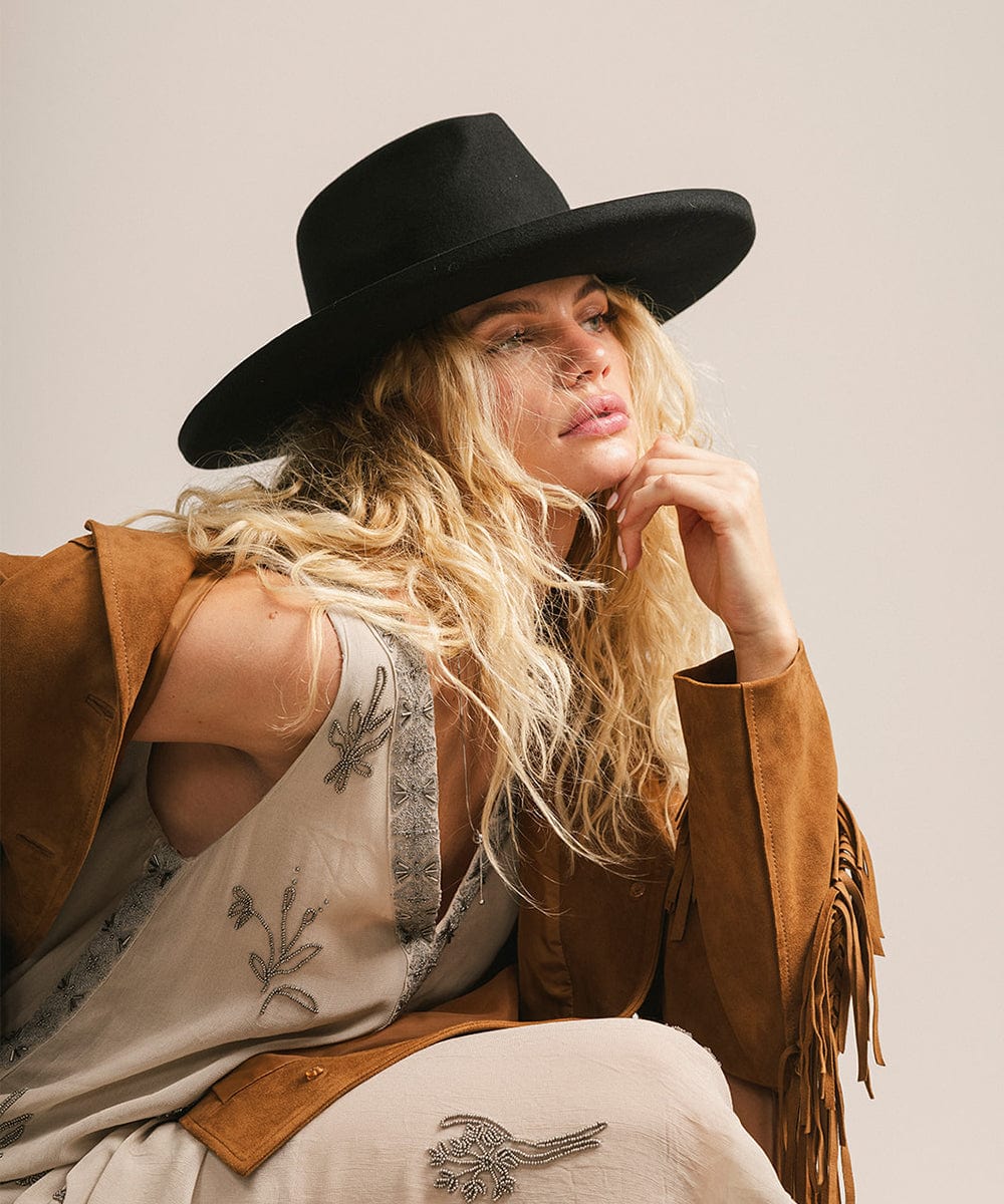 Woman wearing a black hat and brown leather jacket with a neutral background #color_black