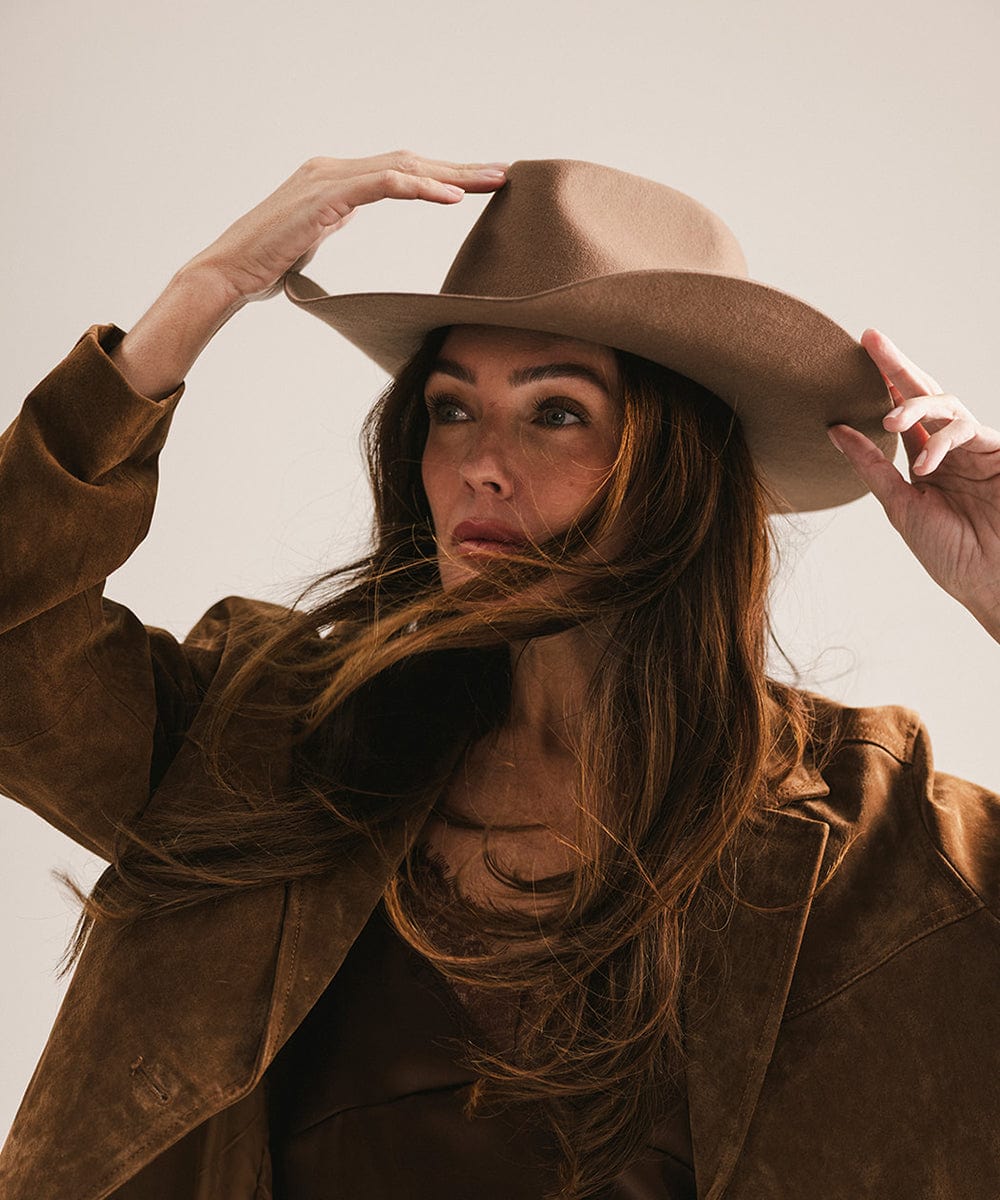 Woman wearing a brown hat and coat against a neutral background #color_chocolate