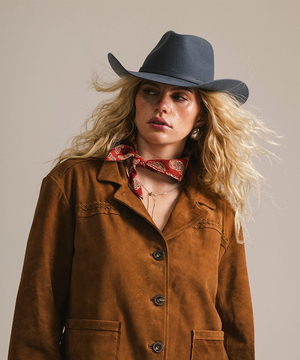 Woman wearing a brown jacket, black cowboy hat, and red patterned scarf against a neutral background #color_vintage blue