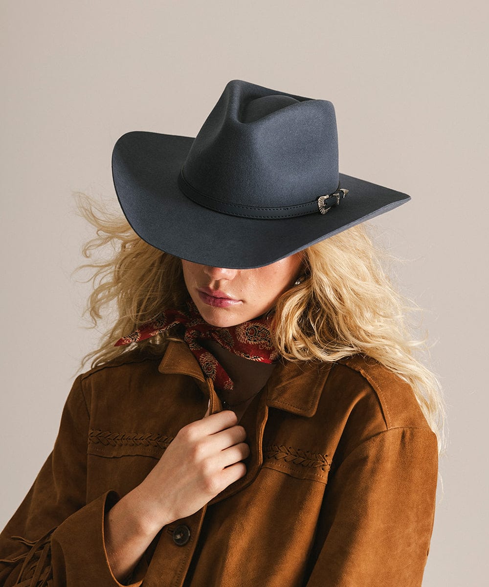 Person wearing a dark blue cowboy hat and brown jacket against a neutral background #color_vintage blue