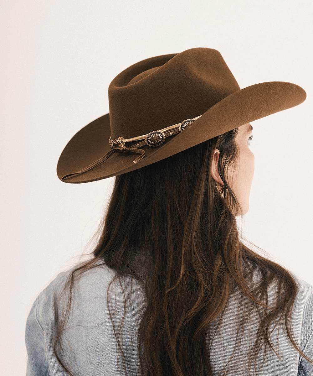 A woman shown from the back wearing a brown felt cowboy hat with a decorative gold-toned band, against a plain light background #color_coffee