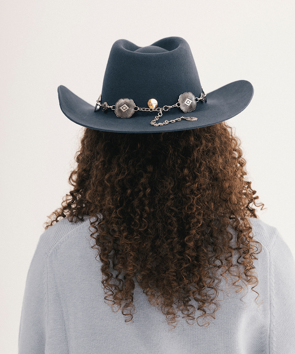 Woman wearing a blue cowboy hat with a concho hat band and a light blue sweatshirt #color_vintage blue