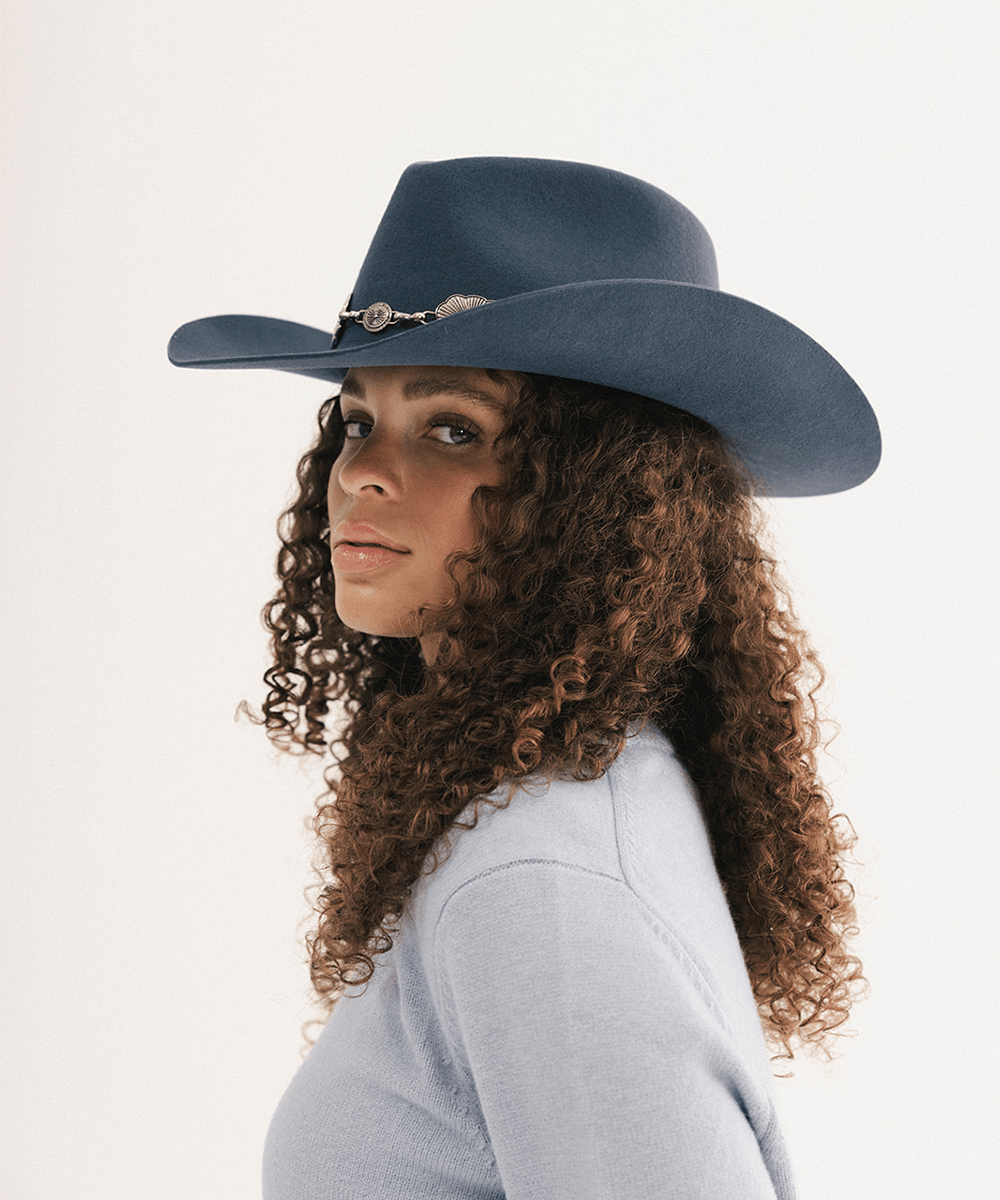 Woman wearing a blue cowboy hat with a concho hat band and a light blue sweatshirt #color_vintage blue