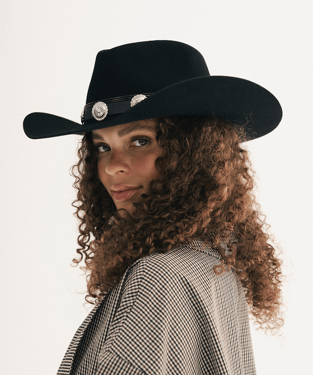 Woman wearing a black cowboy hat with a concho hat band and a plaid shirt #color_black