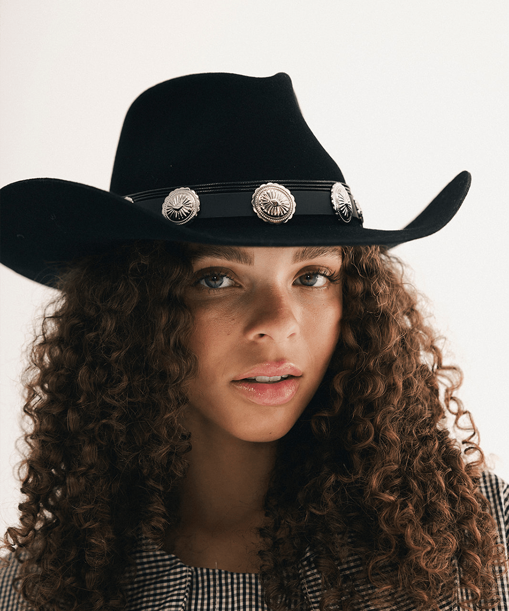 Woman wearing a black cowboy hat with a concho hat band and a plaid shirt #color_black
