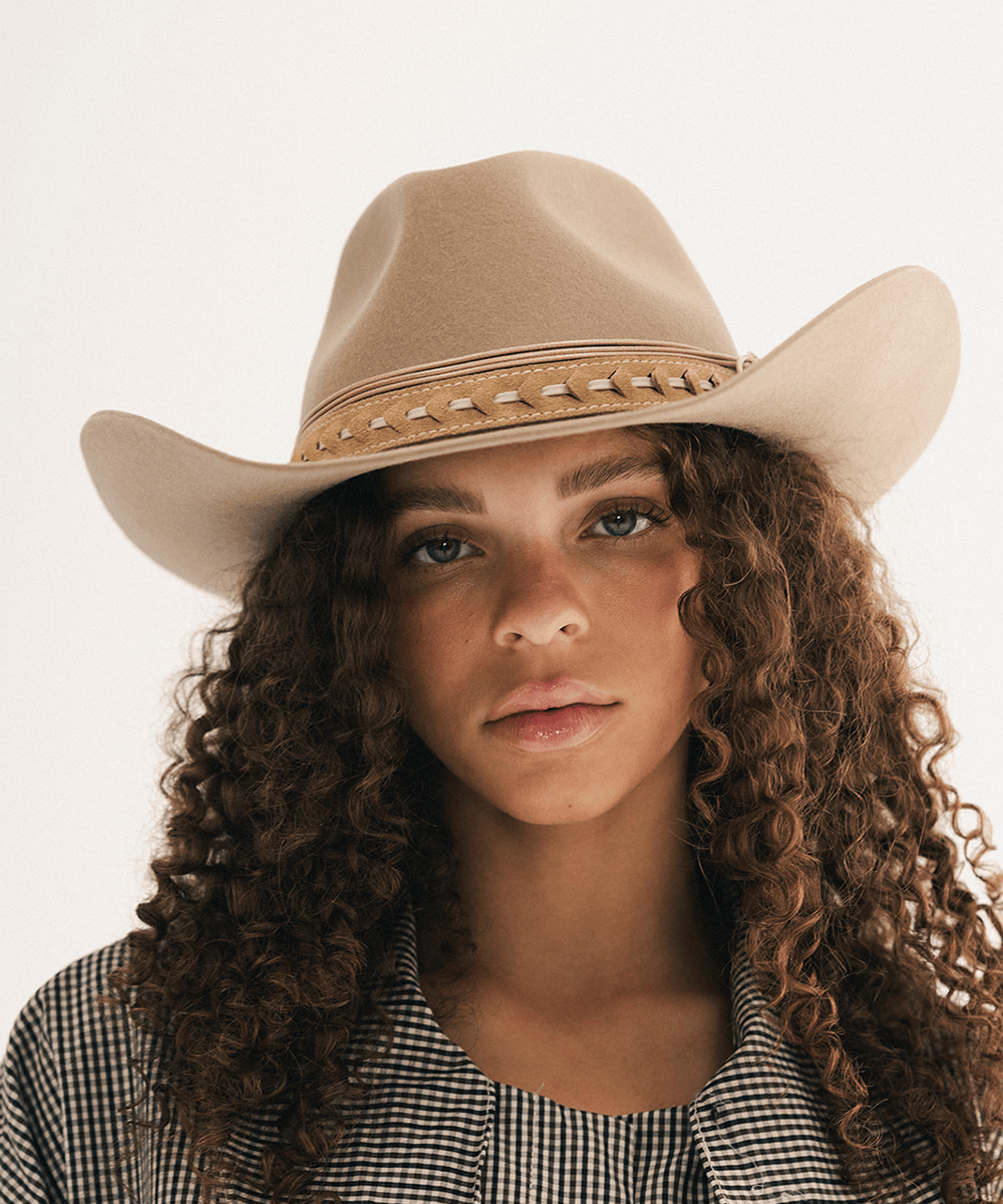 Woman wearing a beige cowboy hat with decorative bands and a plaid shirt #color_tan