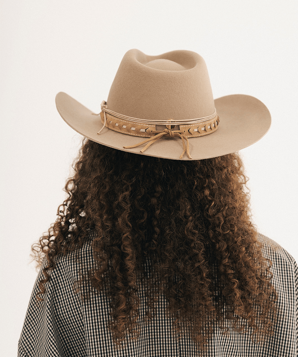 Woman wearing a beige cowboy hat with decorative bands and a plaid shirt #color_tan