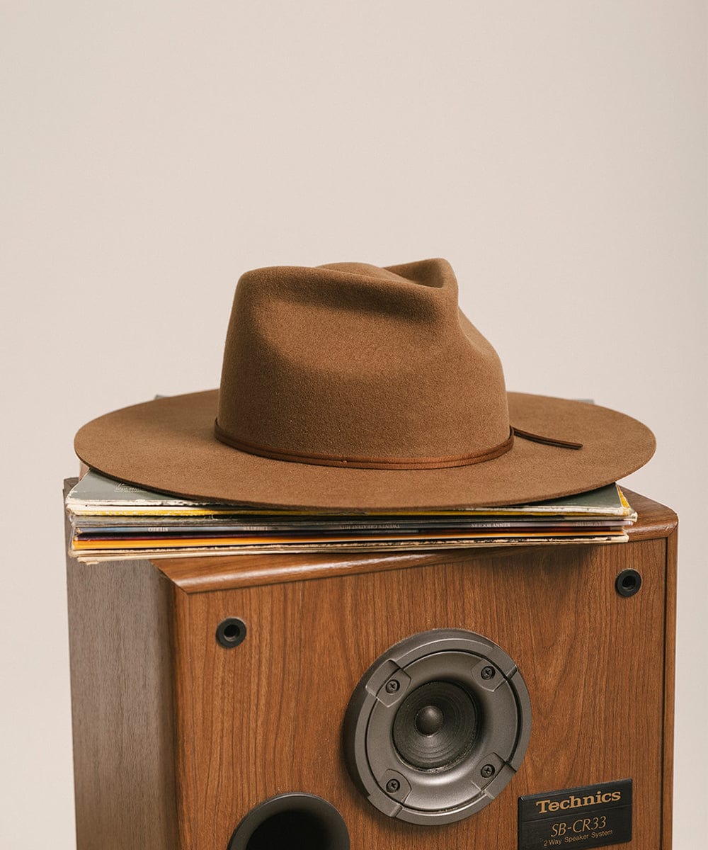 Brown hat on top of a Technics record player with records stacked inside, on a beige background #color_caramel