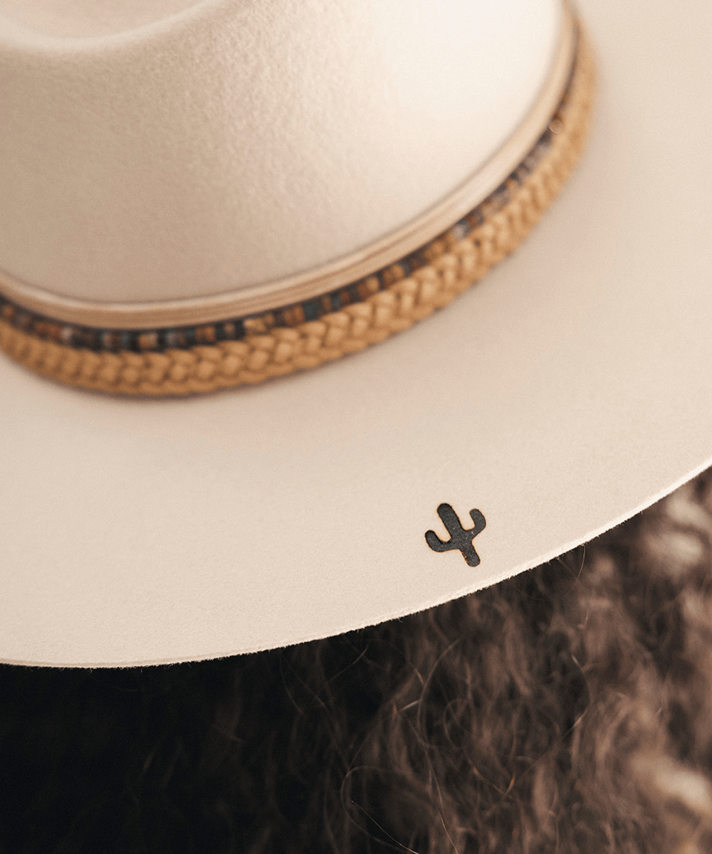 Woman wearing a beige cowboy hat with braided detail against a white background #color_tan
