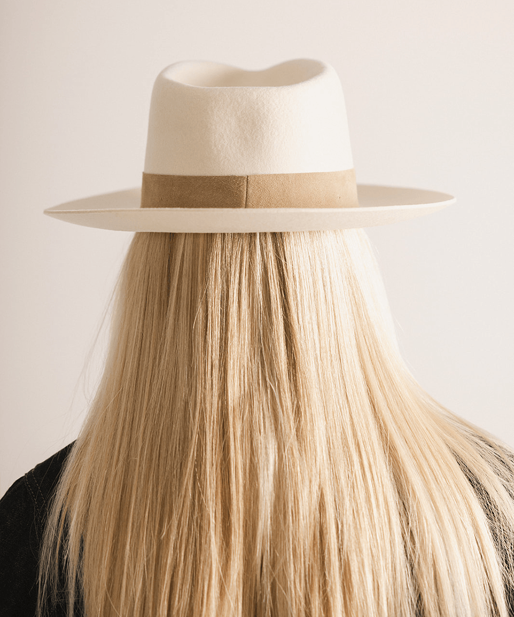 Woman with long hair wearing an off white felt fedora hat with a band against a plain background  #color_off white