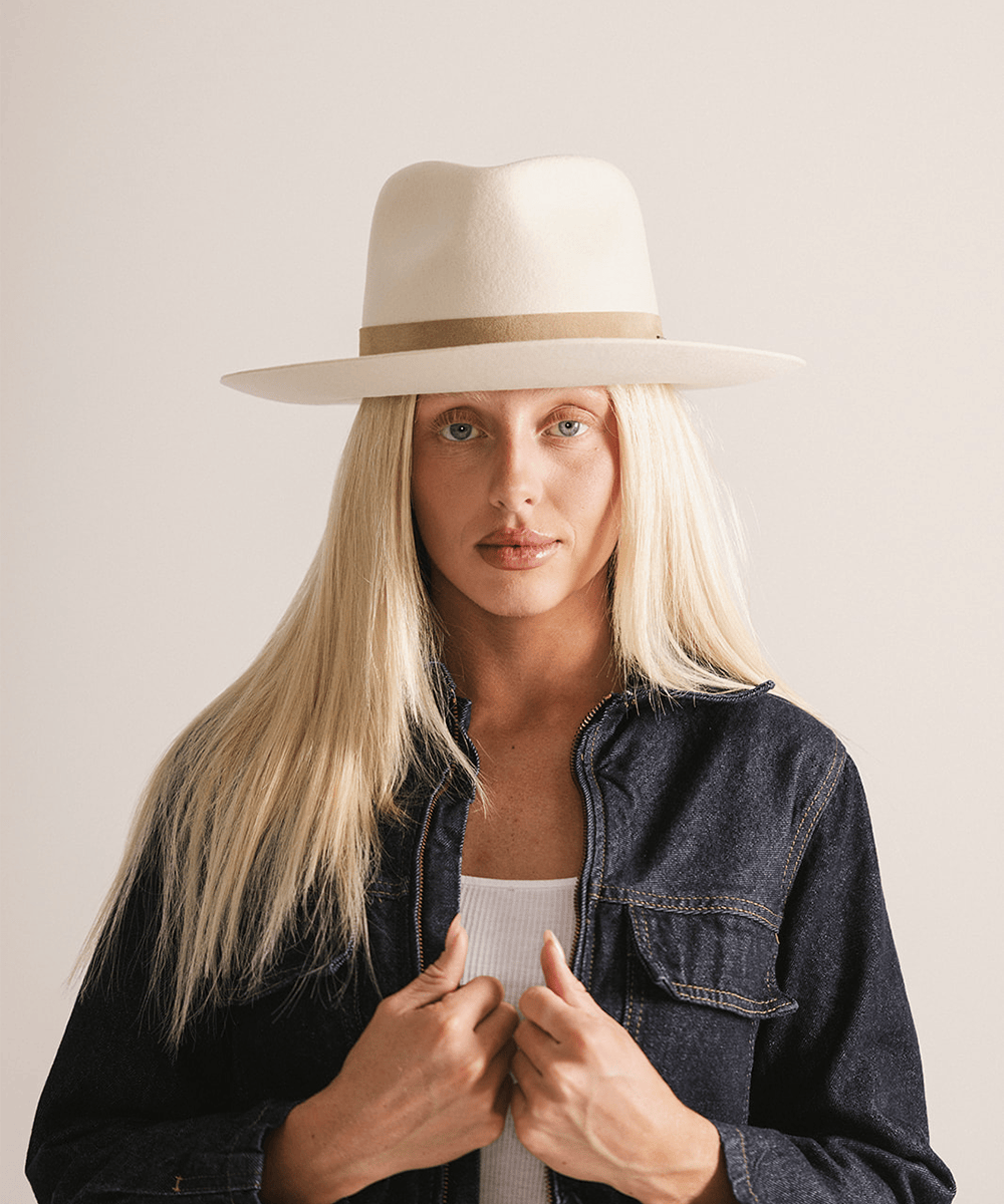 Woman with long hair wearing an off white felt fedora hat with a band against a plain background  #color_off white