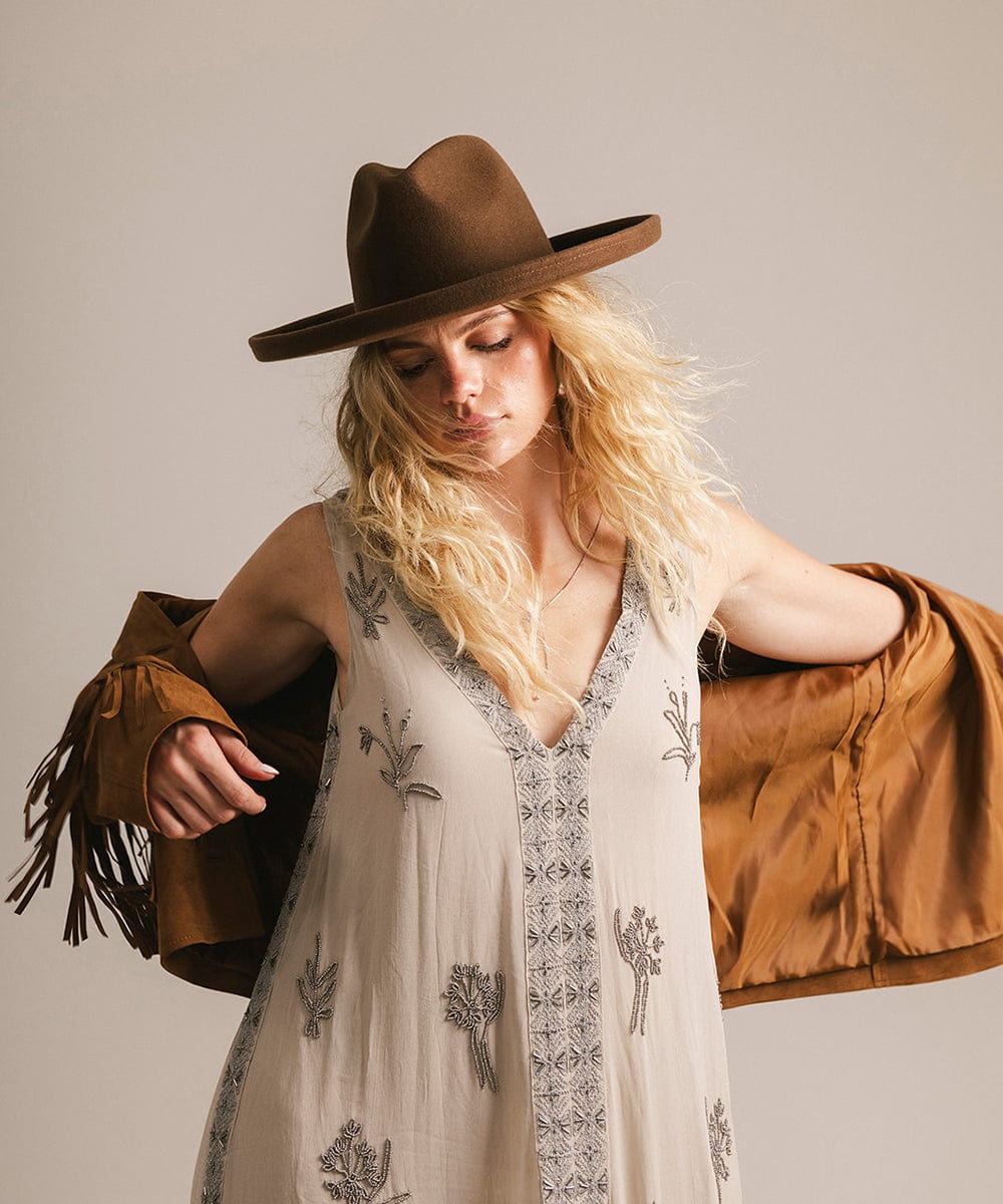 Woman wearing a brown hat and holding a brown jacket against a neutral background #color_chocolate