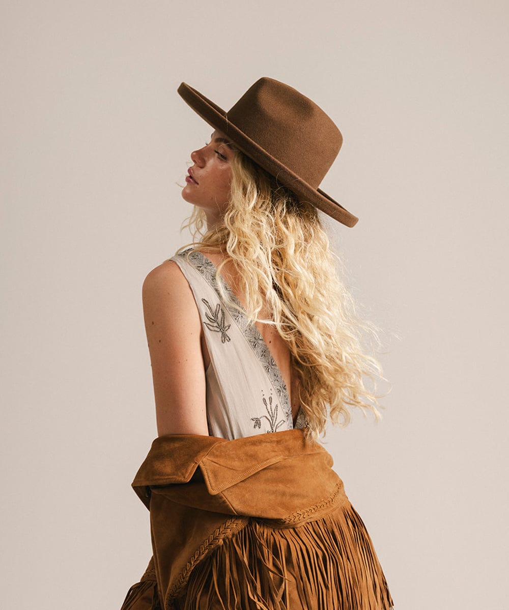 Woman wearing a brown hat and fringed jacket against a plain background #color_chocolate