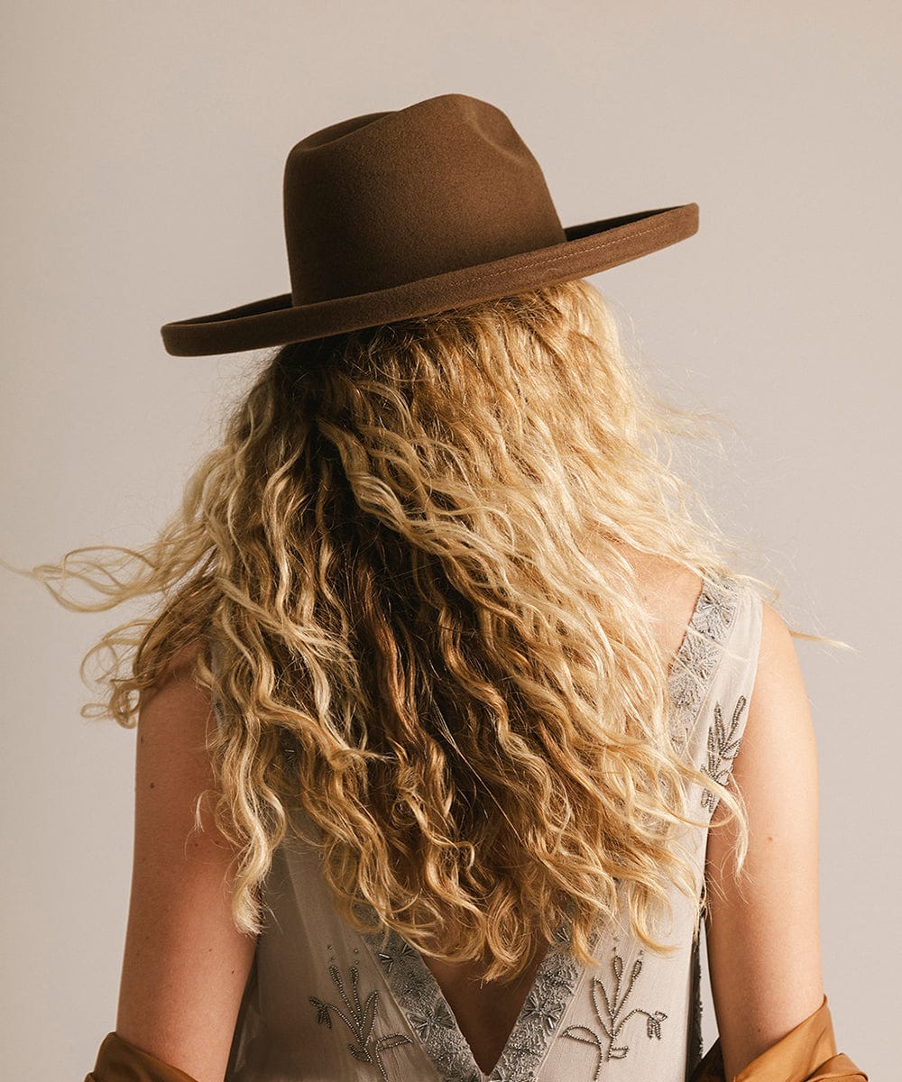 Person wearing a brown wide-brimmed hat with long, wavy hair on a plain background #color_chocolate