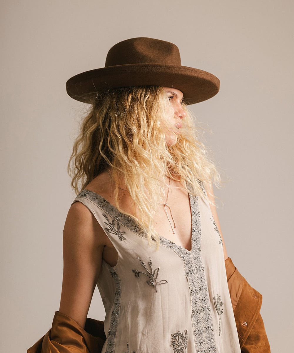 Woman wearing a brown hat and a white embroidered dress against a plain background #color_chocolate