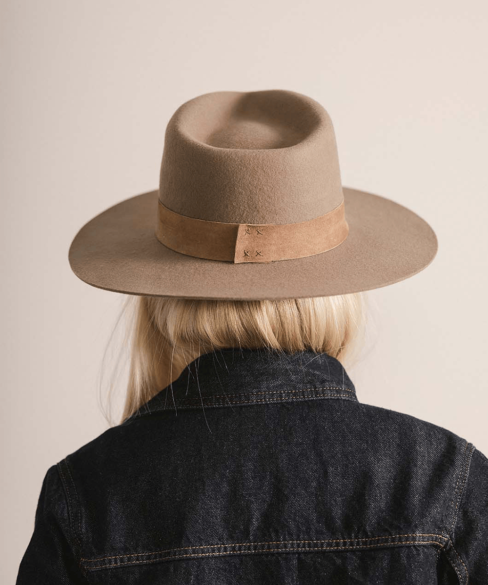 Woman wearing a brown fedora hat with a band against a plain background #color_brown