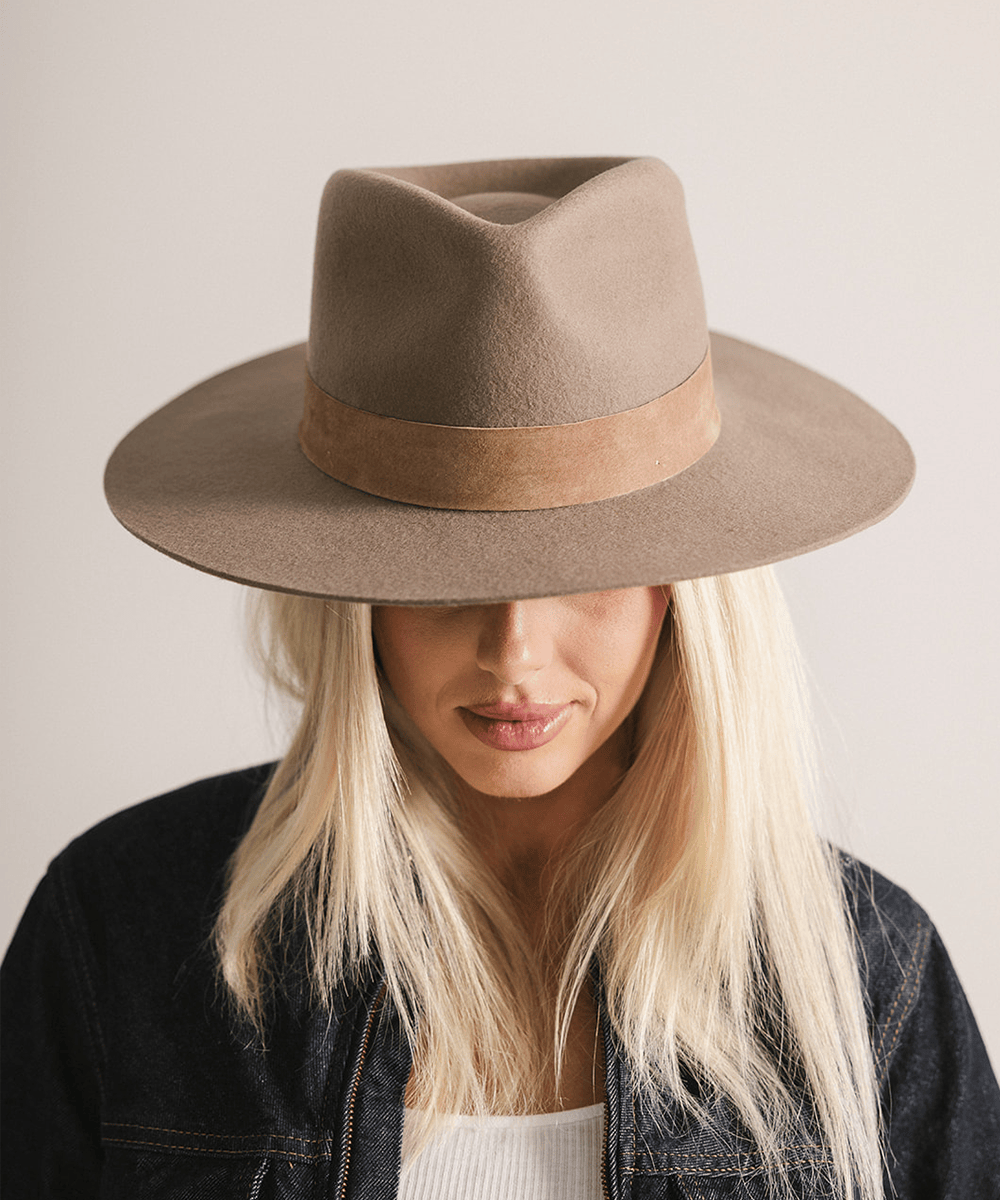 Woman wearing a brown fedora hat with a band against a plain background #color_brown