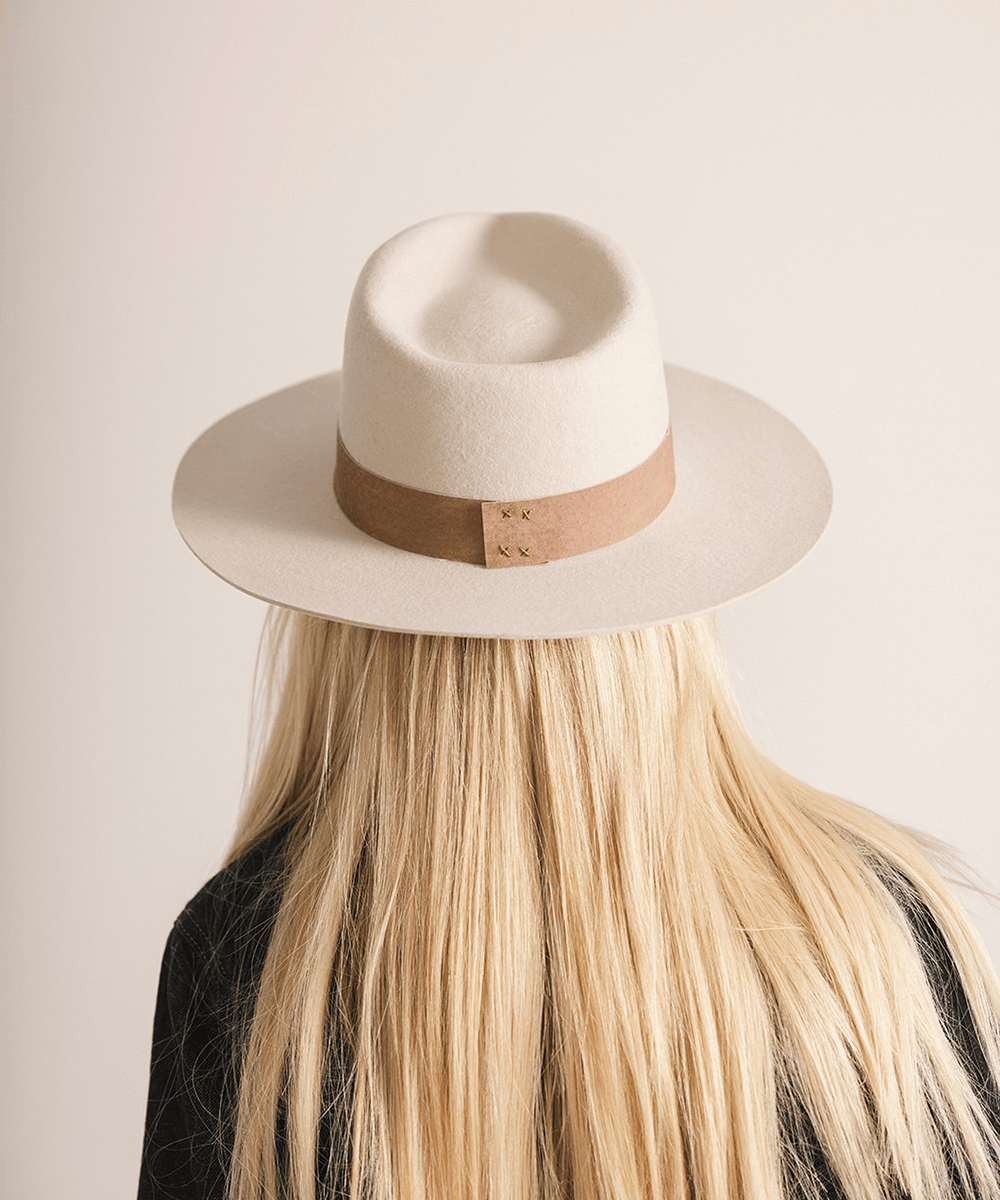 Woman wearing an ivory colored fedora hat with a brown band on a white background #color_ivory