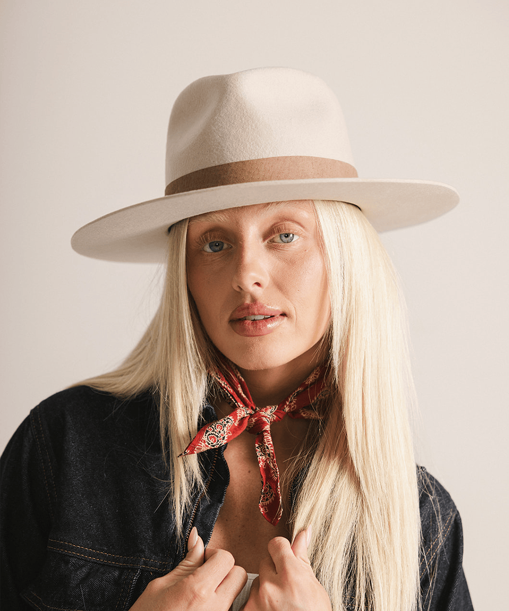 Woman wearing an ivory colored fedora hat with a brown band on a white background #color_ivory