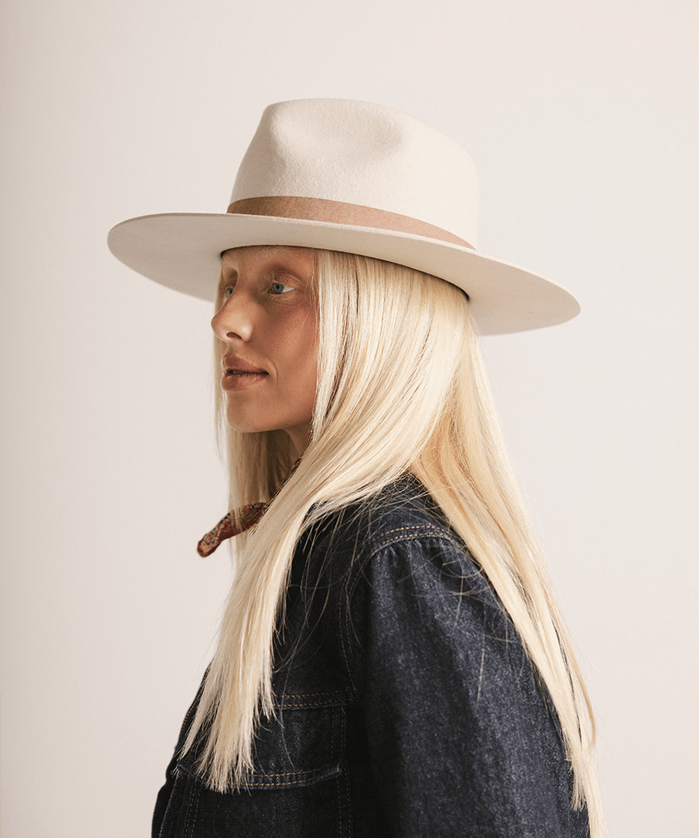 Woman wearing an ivory colored fedora hat with a brown band on a white background #color_ivory