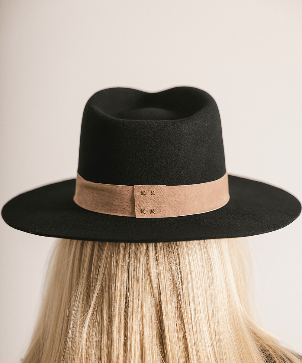 Woman wearing a black fedora hat with a brown band against a white background #color_black-brown