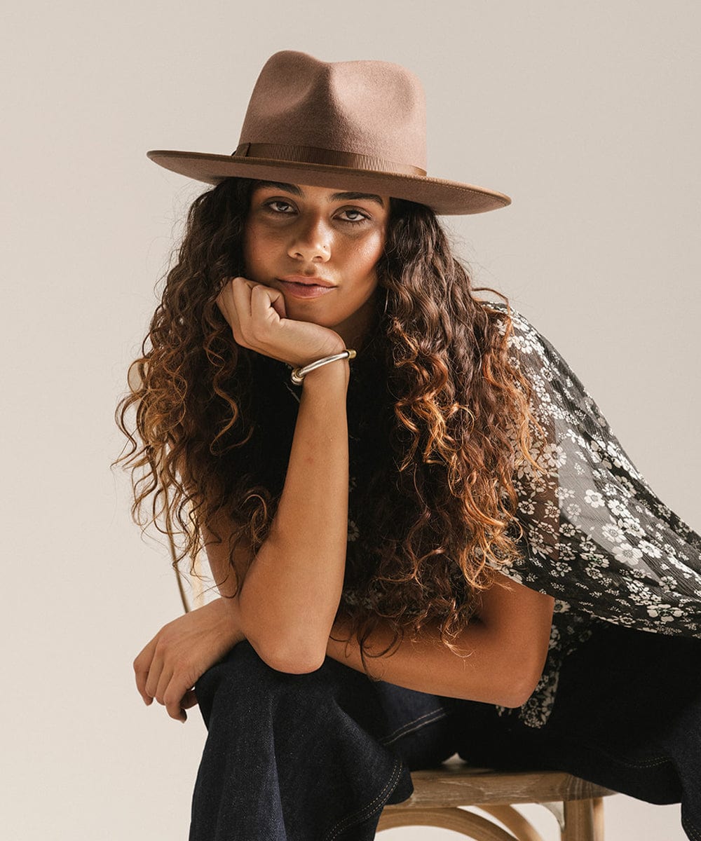 Woman wearing a brown hat sitting on a wooden stool against a plain background #color_chocolate