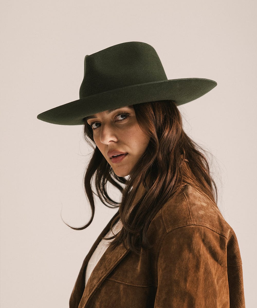 Woman wearing a dark green hat and brown coat against a plain background #color_dark green