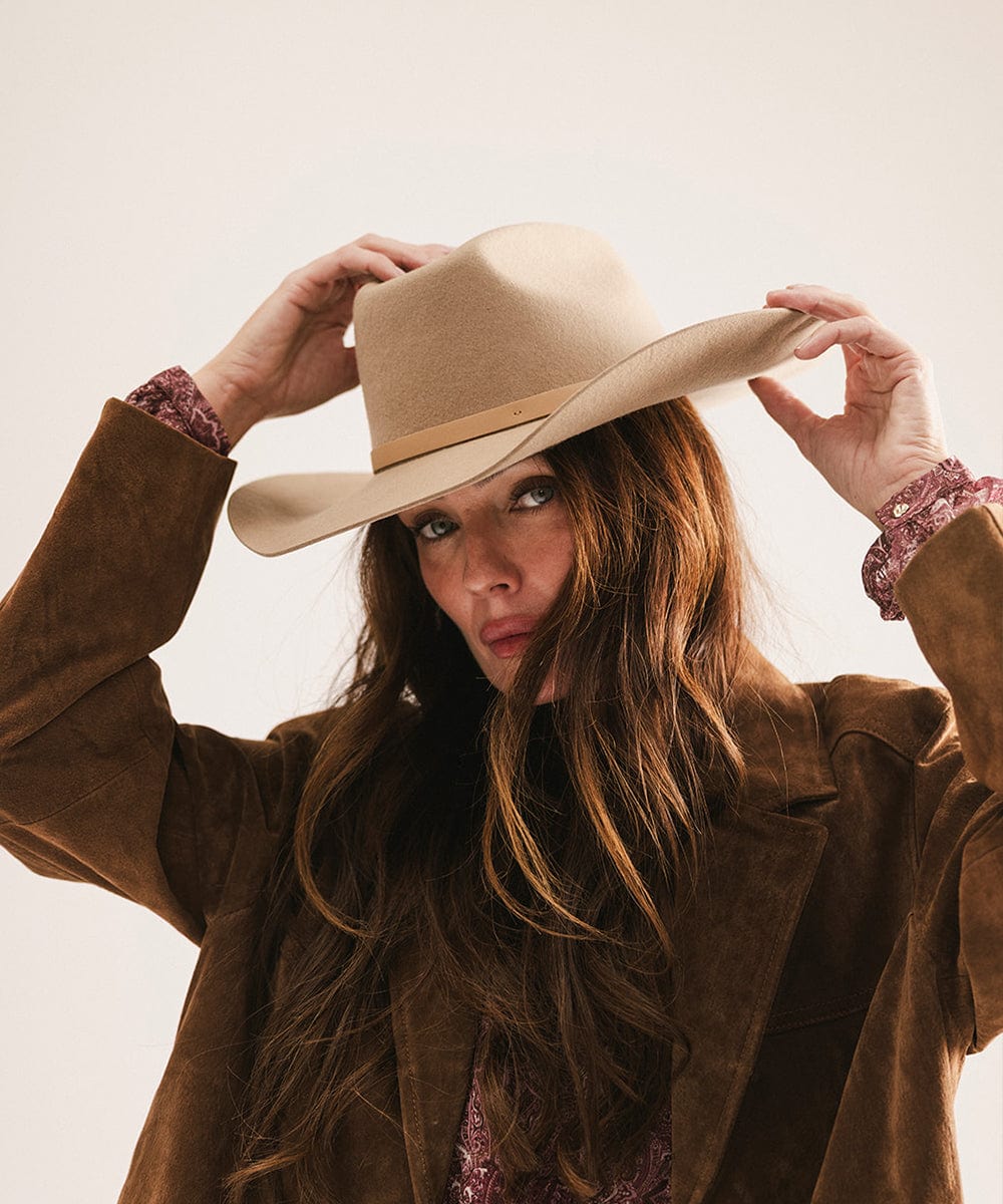 Woman wearing a beige cowboy hat and brown coat against a neutral background #color_tan
