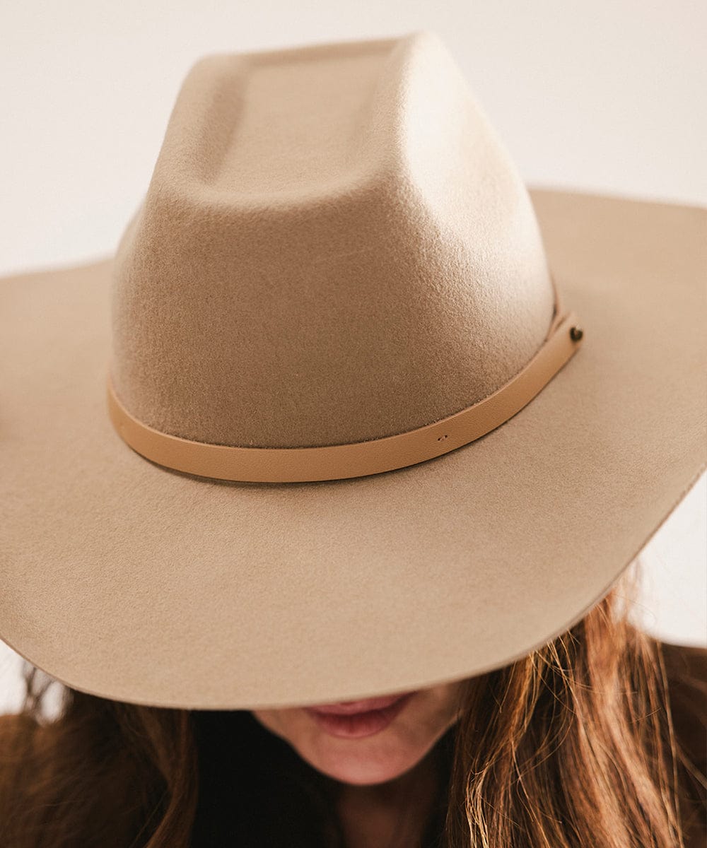 Beige cowboy hat worn by a person with a neutral background #color_tan