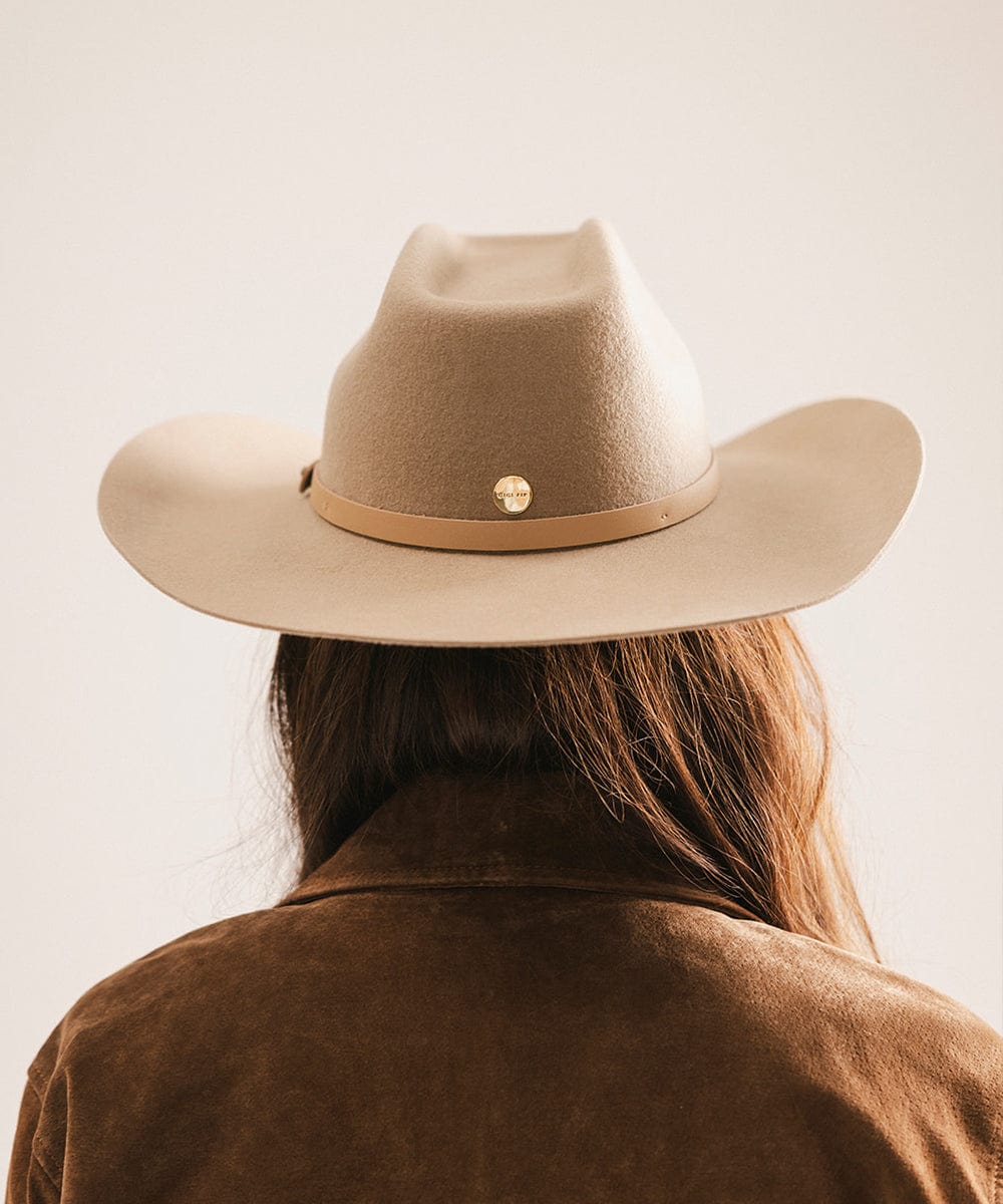 Person wearing a beige cowboy hat with a brown band on a plain background #color_tan