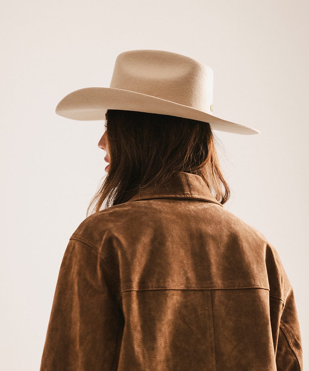 Person wearing a beige cowboy hat and brown jacket on a plain background #color_tan
