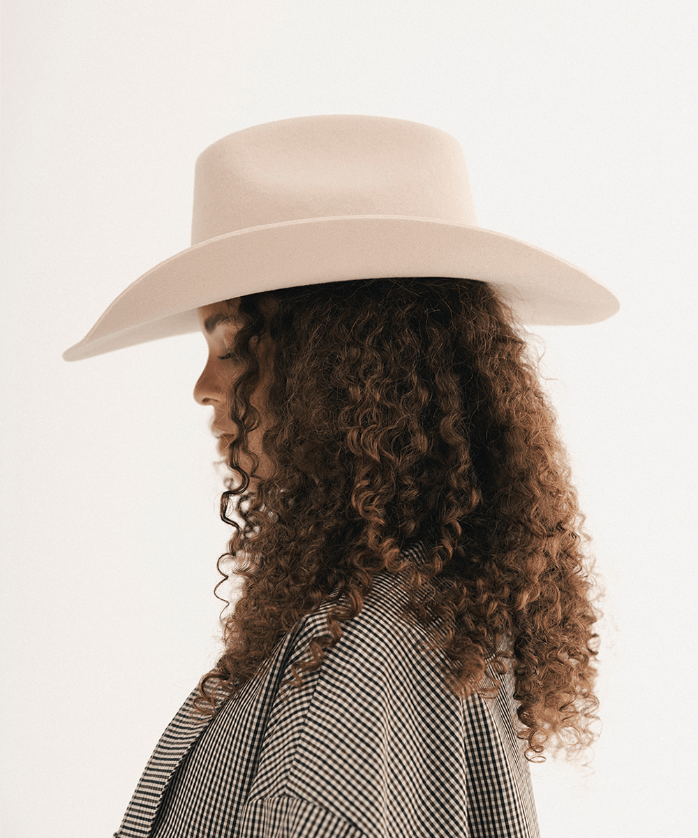 Woman wearing a cream cowboy hat with an upturned brim and an attached cream leather band, plaid shirt on a white background #color_cream