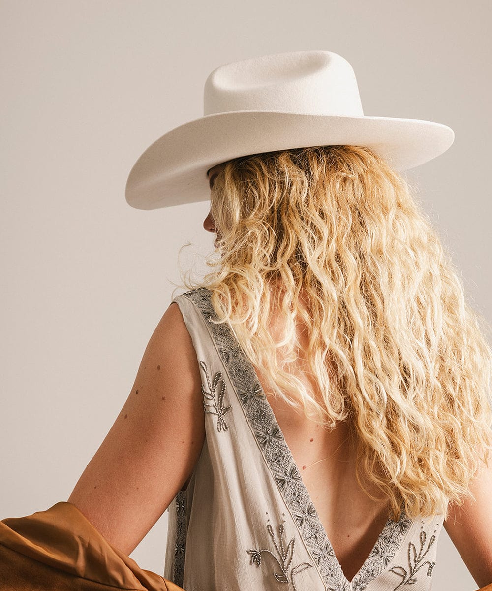 Woman wearing a white cowboy hat and patterned top with a neutral background #color_off white