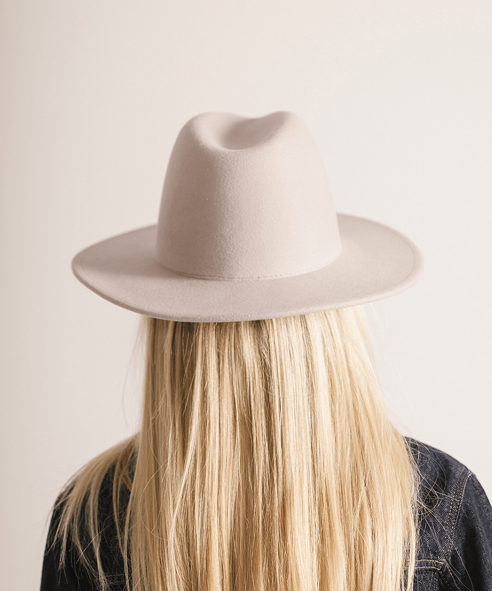 Person wearing an ivory colored fedora hat on a plain background #color_ivory