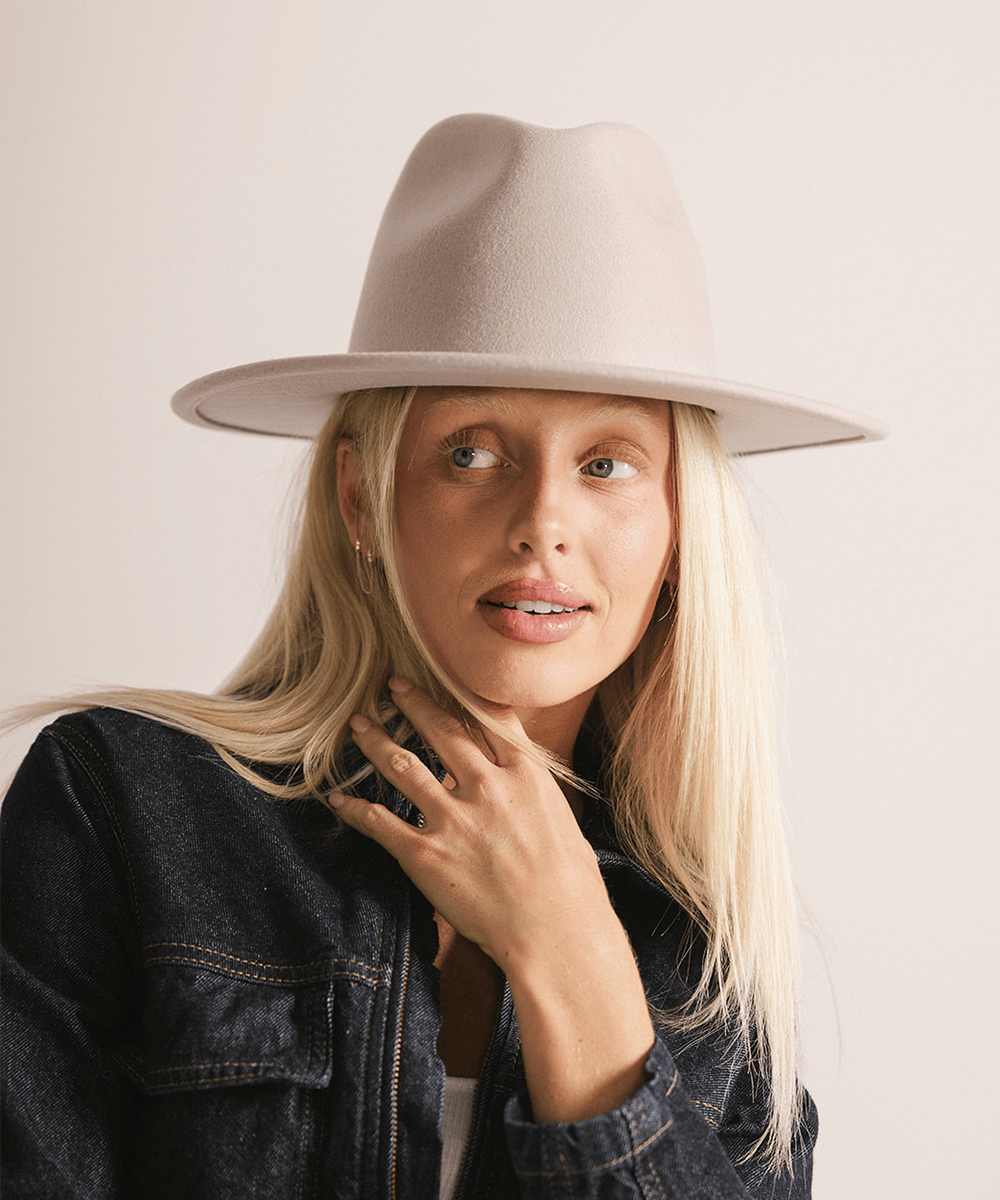 Person wearing an ivory colored fedora hat on a plain background #color_ivory