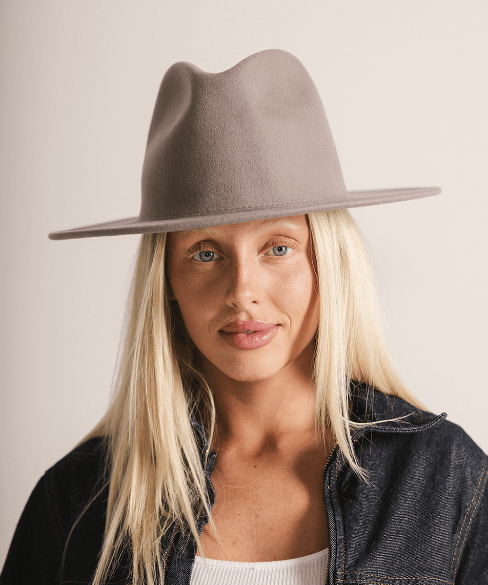 Woman wearing a light grey fedora hat and a dark grey jacket against a plain background #color_light grey