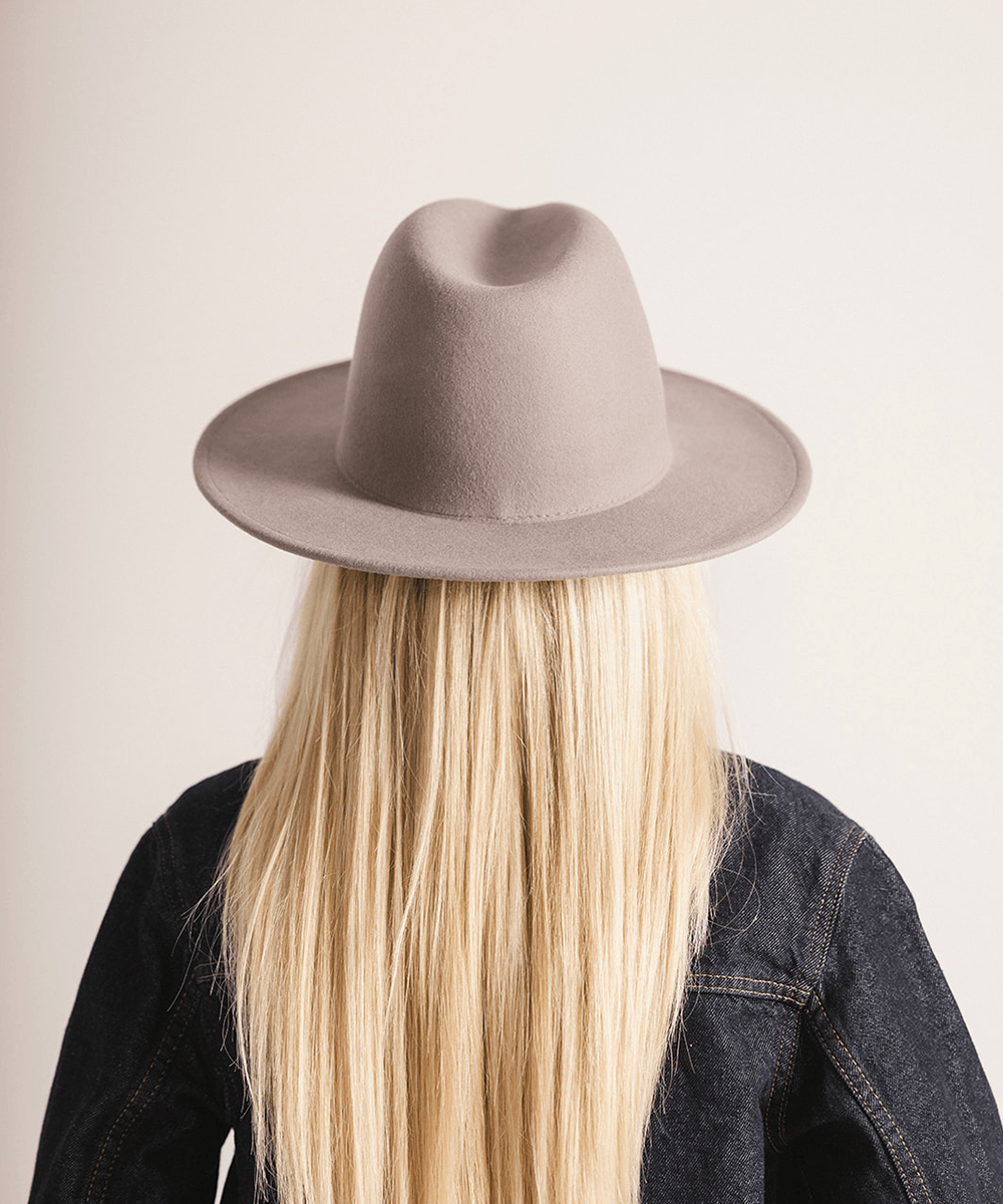 Woman wearing a light grey fedora hat and a dark grey jacket against a plain background #color_light grey