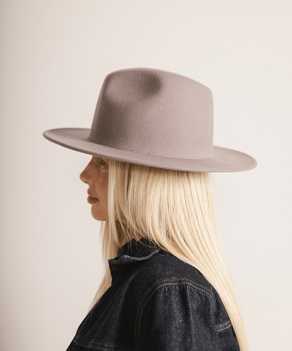 Woman wearing a light grey fedora hat and a dark grey jacket against a plain background #color_light grey