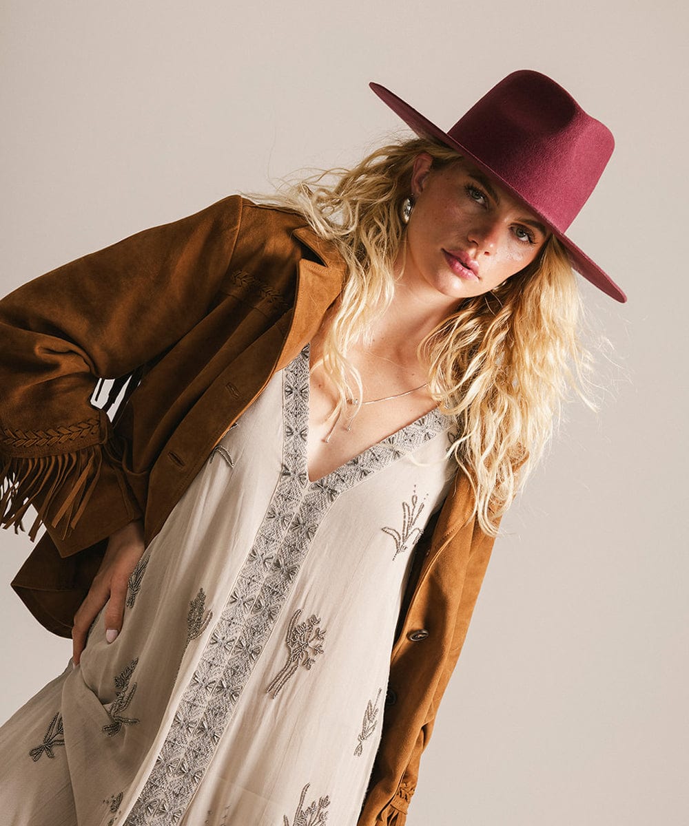 Woman wearing a brown jacket, white dress with black patterns, and a merlot hat against a plain background #color_merlot