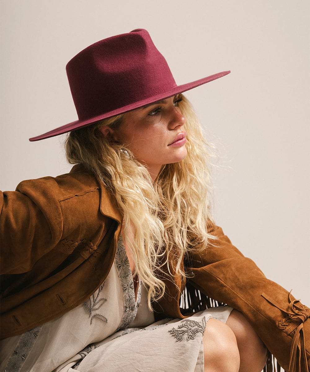 Woman wearing a maroon hat and brown coat against a plain background #color_merlot