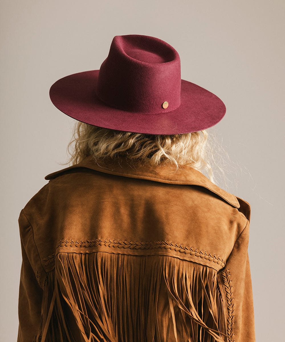 Person wearing a brown fringed jacket and maroon fedora hat on a plain background #color_merlot