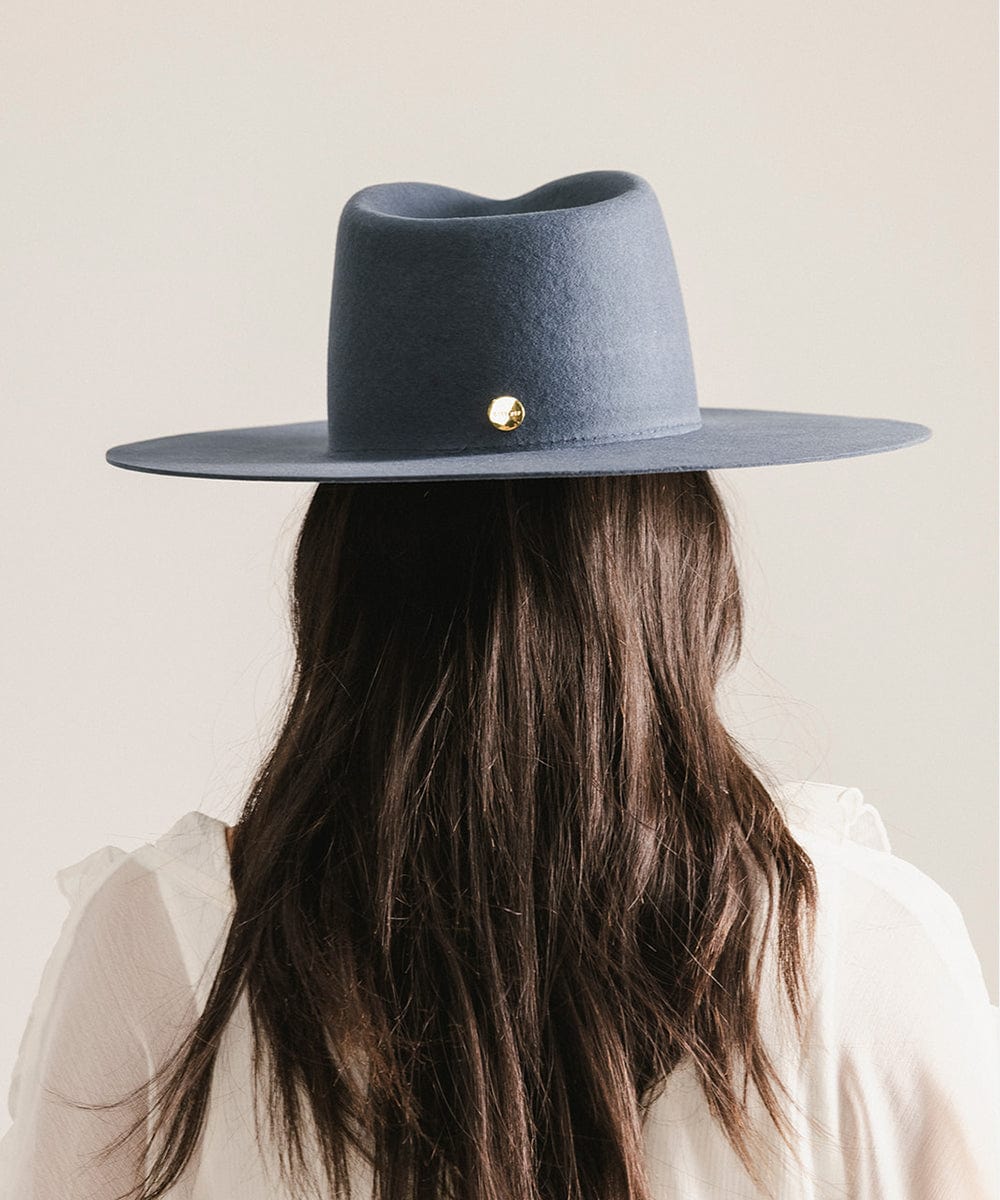 Person wearing a navy blue wide-brimmed hat with a gold button on a light background #color_vintage blue
