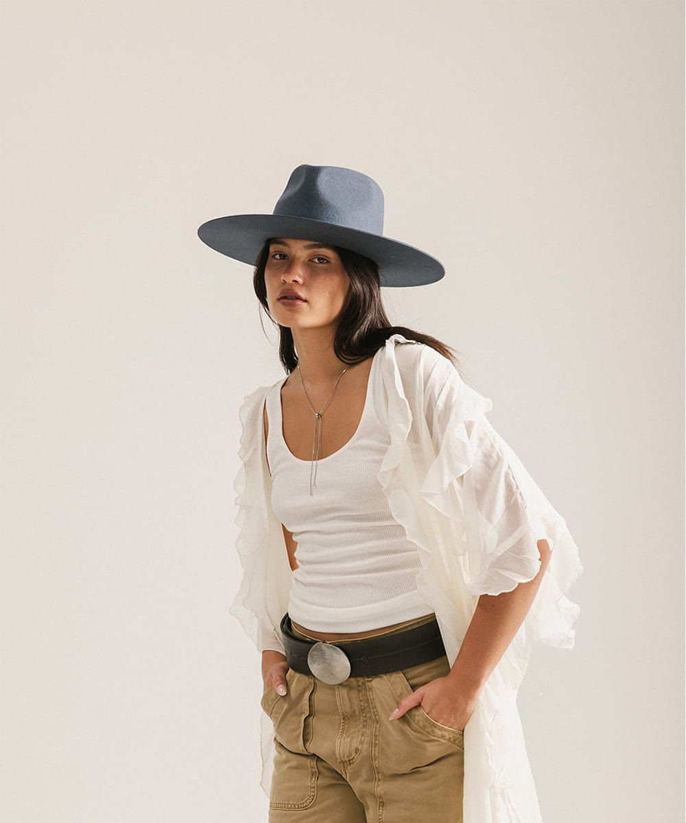 Woman wearing a white top, beige pants, and a blue hat against a plain background #color_vintage blue