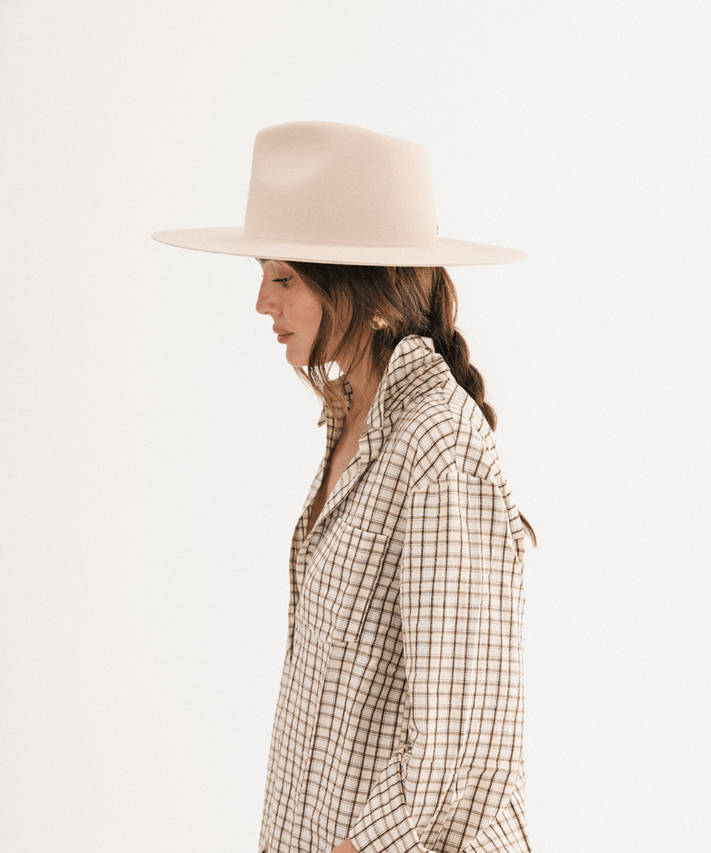 A woman in profile wearing a wide-brimmed light beige hat and a beige plaid button-up shirt, photographed against a clean white studio background #color_cream