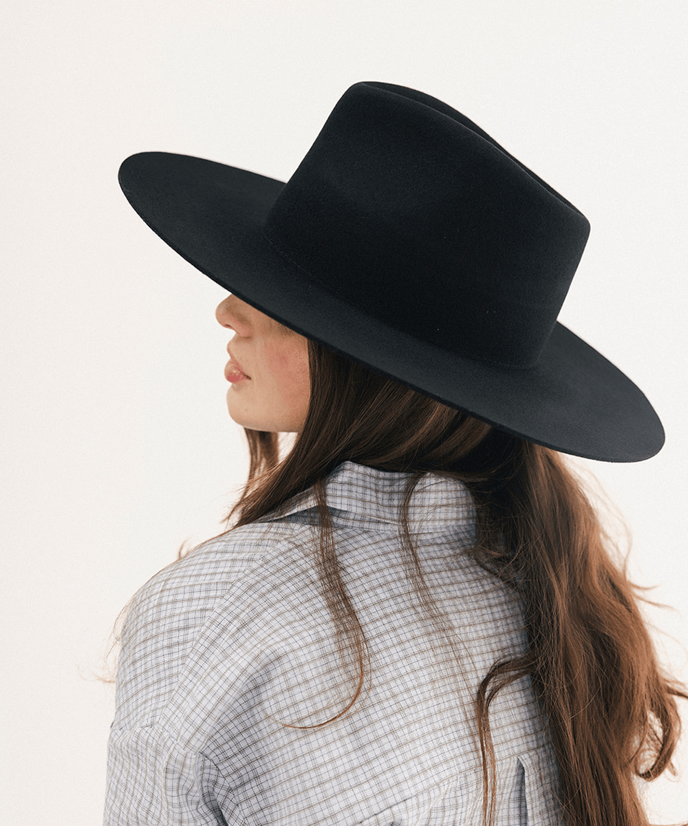 A woman shown from the back and side profile wearing a wide-brim black felt hat and a light gray plaid shirt against a plain white background #color_black