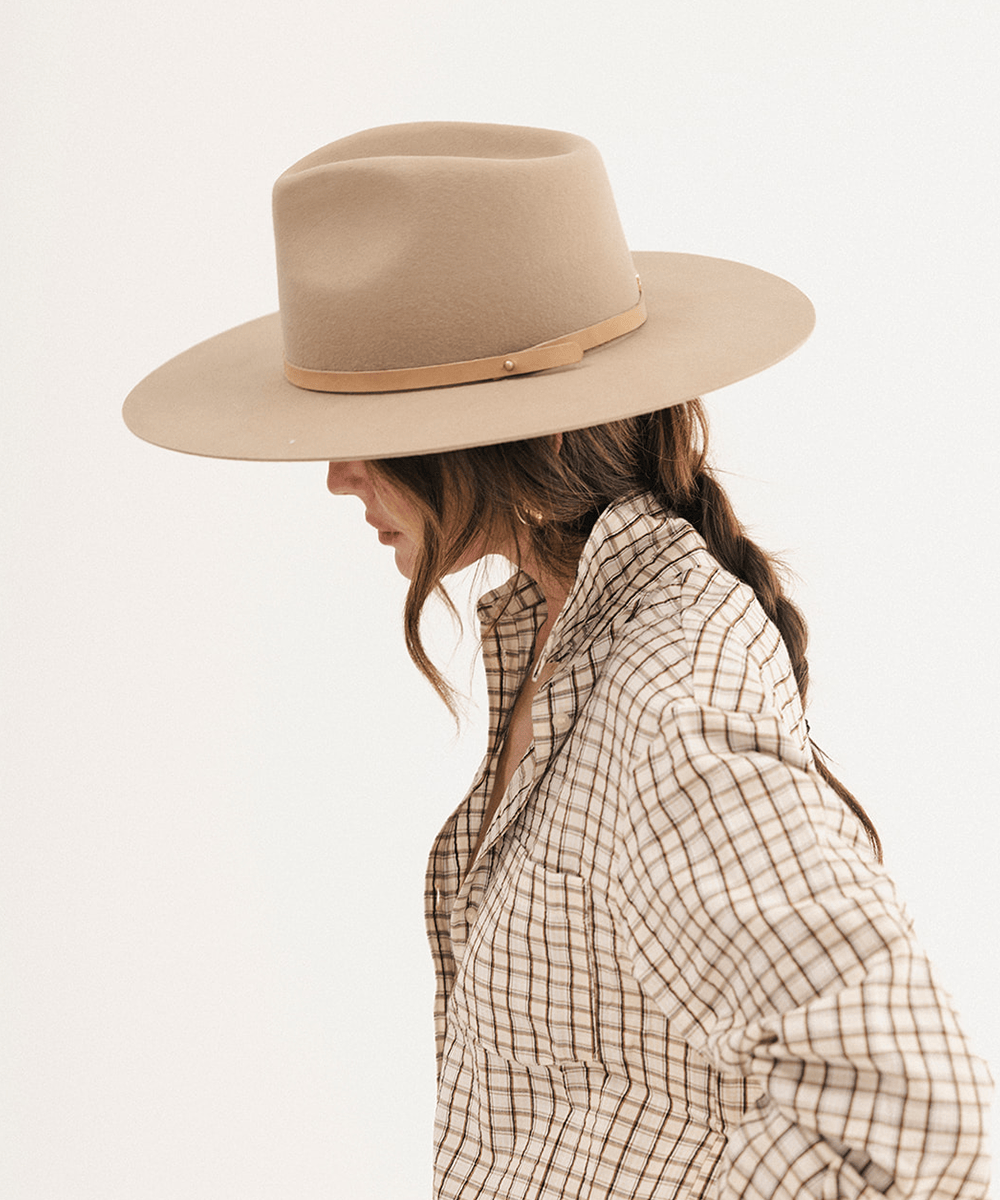 A woman in side profile wearing a beige wide-brim fedora hat with a tan band and a beige-and-brown plaid button-up shirt, photographed against a clean white background #color_tan