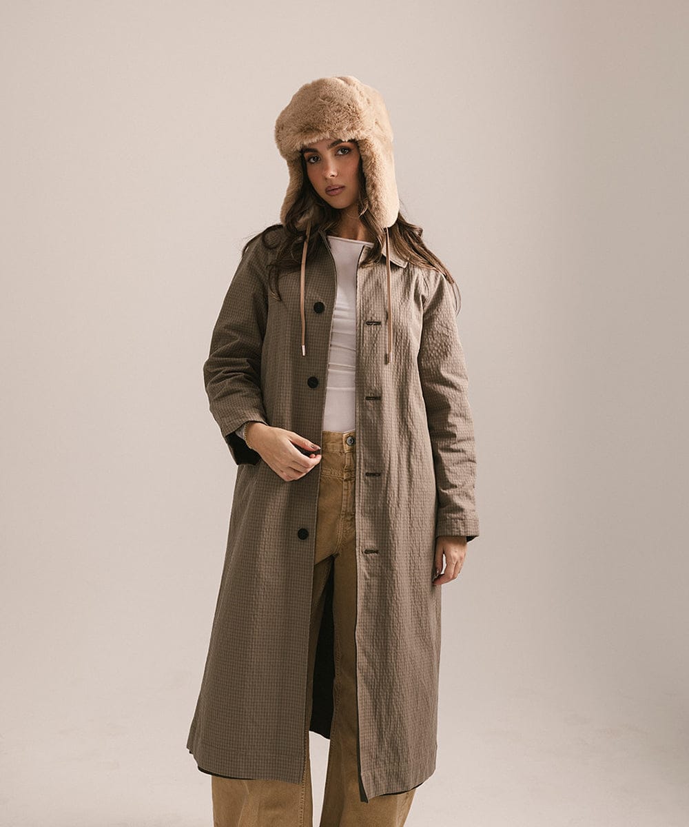 Woman wearing a long coat and fur hat on a plain background #color_tan