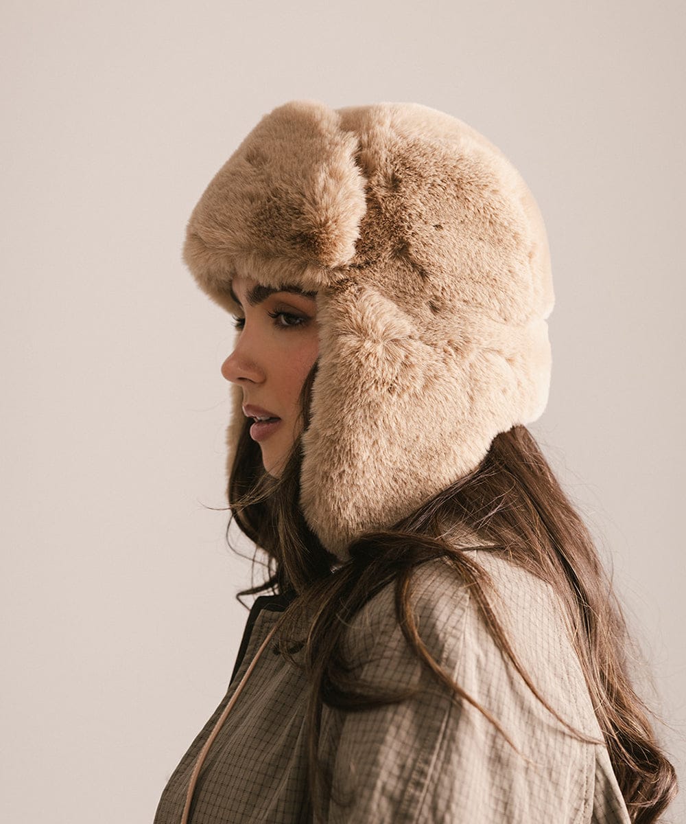 Woman wearing a beige fur hat against a neutral background #color_tan